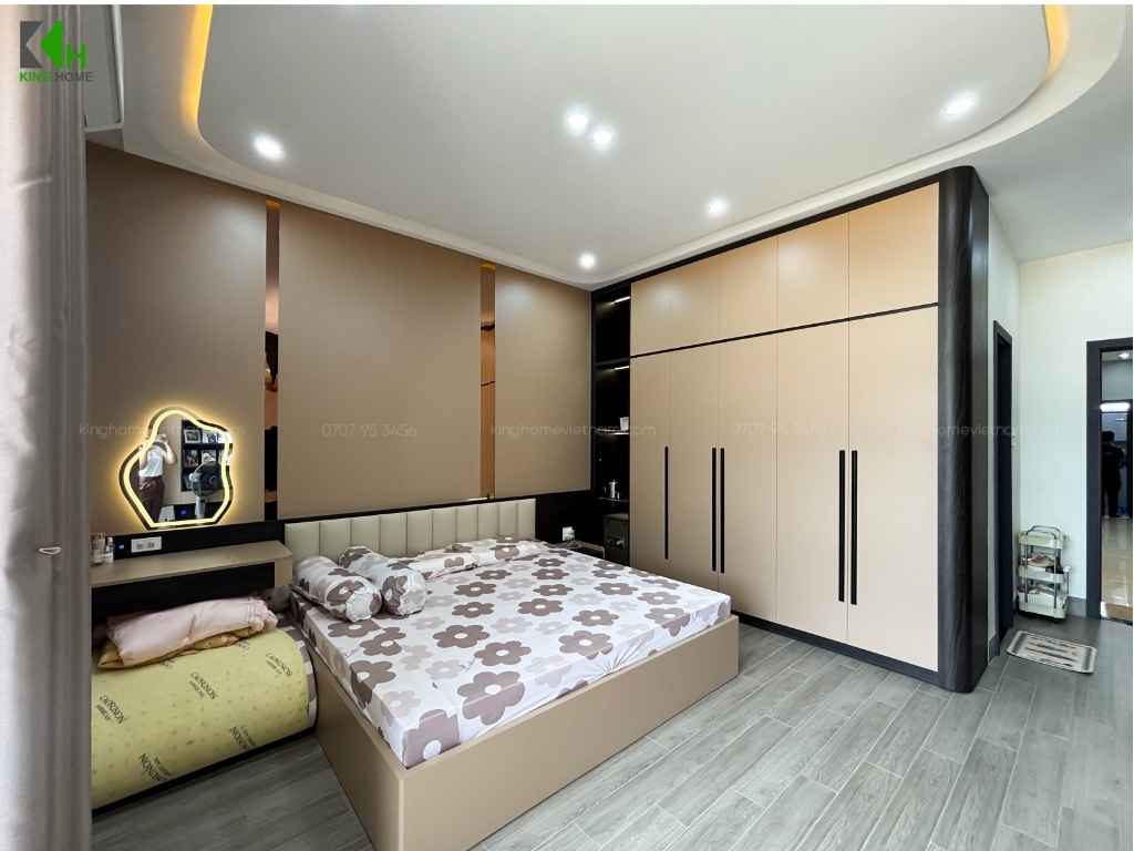 Bao quanh một bên phòng là hệ tủ quần áo kịch trần với cánh tủ màu be sáng, kết hợp các đường viền và tay nắm màu đen tạo sự đồng bộ với nội thất
